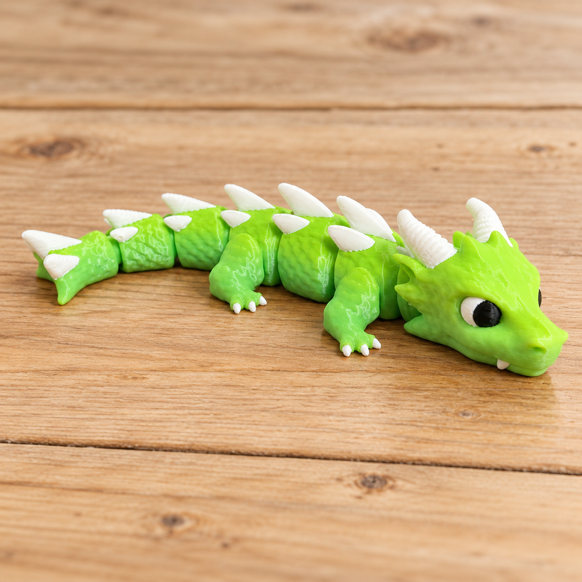 Green articulated Baby Dragon with white horns and spikes on light wood