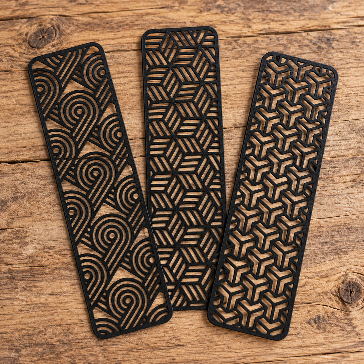 Three black geometric line art bookmarks arranged on a rustic wooden tabletop