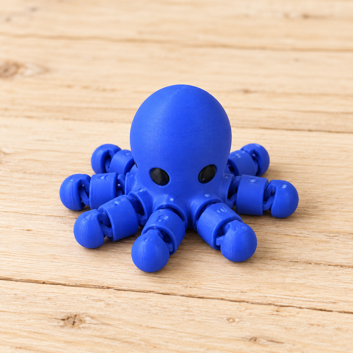 Solid blue articulated Octopus Little Critter with black eyes on light wood