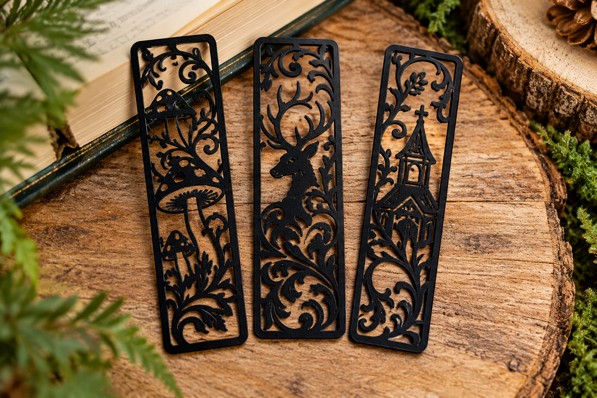 Three forest-themed black bookmarks featuring mushrooms, deer and church on rustic wood